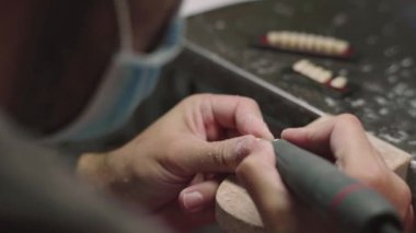 Laboratuvarda diş protezi yaparken seramik dişlerini makineyle cilalayan tanınamayan erkek teknisyenin yakın çekimi.