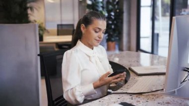 Modern ışık ofisinde çalışırken masabaşında telefonla konuşurken zarif kıyafetli, gülümseyen bir bayan yönetici başka tarafa bakıyor.