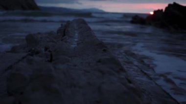 Slow motion view over rocky breakwater against waving sea in twilight at sunset time