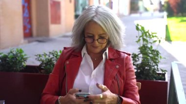 Kafe terasında proje üzerinde çalışırken akıllı telefondan mesajlaşan orta yaşlı kadın girişimci.