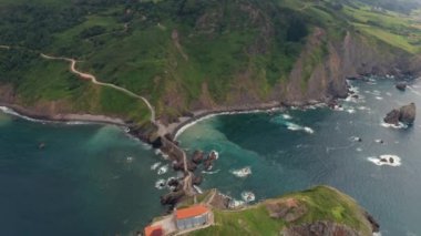 Drone view of paving stone way leading along stone bridge and ridge of rocky hill to lonely house on island Gaztelugatxe surrounded by tranquil sea water under cloudy sky in Basque Country