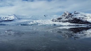 İzlanda 'nın bulutlu bir gününde Vatnajokull Ulusal Parkı' nın volkanik arazisinde karlı dağlarla çevrili denizde yüzen buz parçalarının manzarası.