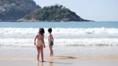 Kız ve erkek kardeşin denize yakın ıslak deniz kıyısında zıplamasını tüm vücuduyla izleyebilirsin.