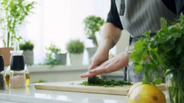 Gerçek zamanlı yüksek açılı, bıçaklı, yeşil maydanoz yapraklı, mutfakta yemek pişirirken tahta kesme tahtasıyla tanınmayan bir kadın.