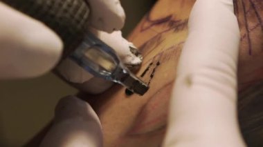 Stüdyoda genç bir kadının koluna dövme yapan dövme sanatçısı.
