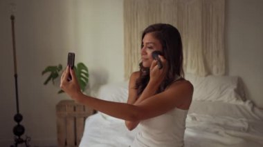 Pijamalı güzel esmer kız akıllı telefonuyla selfie çekiyor.