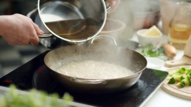 Önlüklü tanınmayan kadın aşçı pilav pişirirken tavada tavuk suyu ve pilav ekliyor.