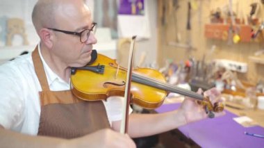 Side view of mature male artisan luthier testing violin after restoration in workshop