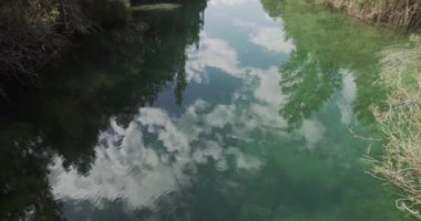 Sakin yüzeyi sulara yansıyan yeşil tepelerle çevrili huzurlu göl manzarası.