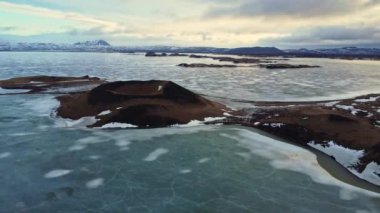 İzlanda 'da bulutlu bir kış akşamında Myvatn Gölü kıyısında karla kaplı Skutustadagigar sahte kraterlerinin insansız hava aracı görüntüsü 
