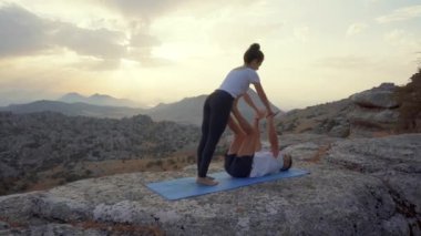 Odaklanmış erkek ve kadının akro yoga çalışmalarını ve kayalık dağın tepesinde Front Plank Asana hareketlerini tüm vücuda yansıtıyor.