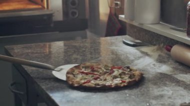Lokanta mutfağında pişirdikten sonra sıcak fırından kürekle pizza alan isimsiz bir pizzacı.