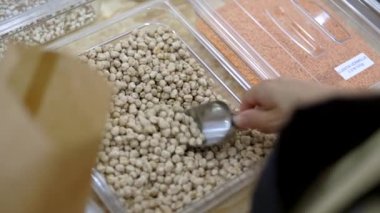 Dükkan sahibi yerel bir dükkanda cam kavanozun içine çiğ nohut koyuyor.