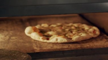 Kimliği belirsiz pizzacı sıcak fırın açıyor ve restoran mutfağında yemek pişirirken pizzayı kürekle çeviriyor.