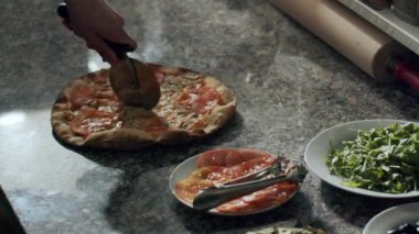 Anonim pizza üreticisi restoran mutfağında çalışırken taze pişmiş iştah açıcı sıcak pizzayı mermer tezgahta kesiyor.