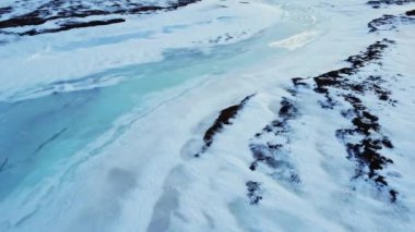 İzlanda 'nın dağlık bölgelerindeki soğuk kış gününde engebeli volkanik yüzeyi kaplayan mavi buz ve beyaz karın drone görüntüsü