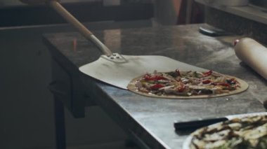 Metal kürekli isimsiz bir aşçı geleneksel İtalyan çiğ pizzasını mermer masa üstünden restoran mutfağında pişirmek için fırına götürüyor.
