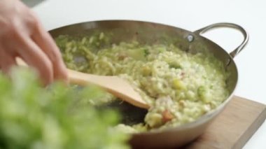 Tavada kızardıktan sonra kremalı ve ahşap spatulayla lezzetli risotto servis eden yüksek açılı bir aşçı.