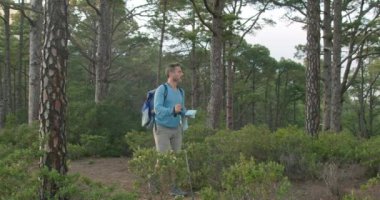 Sırt çantalı ve bastonlu bir adam hafta sonu ormanda yürüyüş yaparken kağıt haritayı inceliyor.