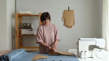 Işık atölyesinde özel ekipmanlarla çalışırken kumaş üzerinde şablon oluşturan ölçüm bandıyla odaklanmış profesyonel terzi.