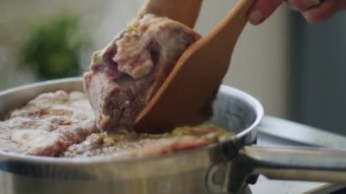 Gerçek zamanlı tahtadan spatulaları olan, mutfaktaki elektrikli ocakta, paslanmaz tavada ossobuco pişiren isimsiz bir insan.