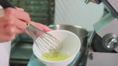 Yüzü olmayan fırıncı mutfakta duruyor ve fırında pişirirken çırpılmış yumurta çırpıyor.