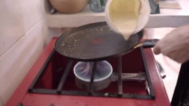 Tanımlanamayan kadın aşçı sıcak tavaya hamuru ekliyor ve evde lezzetli krepler hazırlıyor.