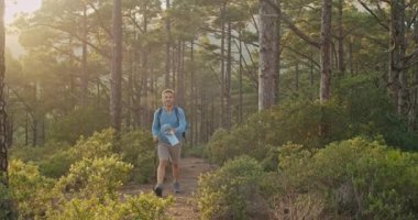 Sırt çantalı ve bastonlu yetişkin bir adamın gündüz vakti yeşil ağaçlıklarda yürüyüş yaparken fotoğrafını çekiyorum.