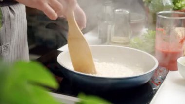 Mutfakta fırında yemek pişirirken tavada ahşap spatulayla acılı risotto karıştıran isimsiz bir şef.