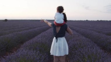 Tanımlanamayan, sevgi dolu bir annenin kucağına aldığı, elinde mor lavanta çiçekleriyle çiçek açan bir tarlada durup günbatımının tadını çıkarırken,
