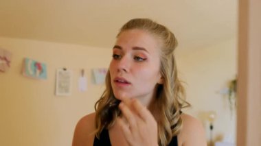 Genç kız aynaya bakıyor ve rujla makyaj yapıyor.