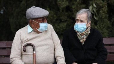 Yaşlı bir çiftin, bir kış öğleden sonra gözlerini kaçırırken sokakta maske takması ön planda.
