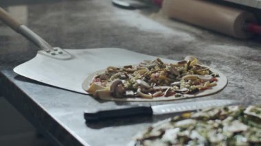 Metal kürekli isimsiz bir aşçı geleneksel İtalyan çiğ pizzasını mermer masa üstünden restoran mutfağında pişirmek için fırına götürüyor.