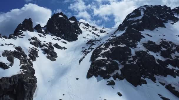 晴れた日のシエラ グレドスの地域公園の暗い岩で雪の斜面を下りる遠隔スキーヤー — ストック動画