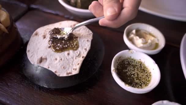 在黎巴嫩的餐馆里 一个高角形的无名男子在餐桌上的扁平面包上涂上传统的扎塔尔酱汁 配上开胃的葡萄叶和薯条 — 图库视频影像