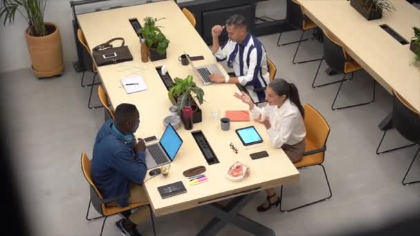 ネットブックとタブレットを閲覧する多民族の同僚の上から 現代のオープンスペースオフィスで一緒に作業中にテーブルに座っている間 — ストック動画