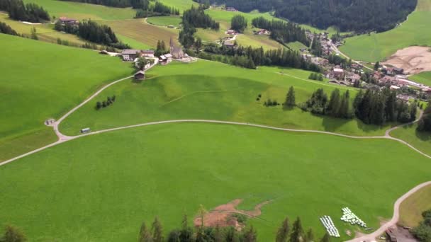 イタリアの絵のようなドロマイトアルプスの緑の草の丘の斜面に位置する小さな村の平和な空中風景 — ストック動画