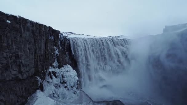 Zoom sur drone vue de la cascade propre tombant de falaise enneigée par une journée froide d'hiver dans la nature de l'Islande