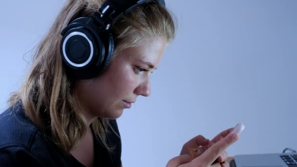 积极的年轻女性一边用耳机听音乐 一边用智能手机和朋友聊天 同时在家里消磨时光 — 图库视频影像