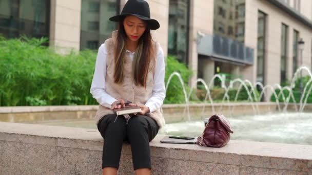 도시에서 테이크 커피와 분수의 경계에 앉아있는 노트북에 모자에 히스패닉 여성의 — 비디오