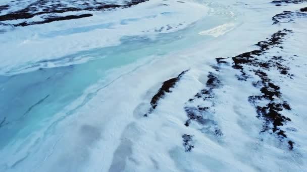 アイスランド高地の寒い冬の日に不均一な火山の表面を覆う青い氷と白い雪のドローンビュー — ストック動画