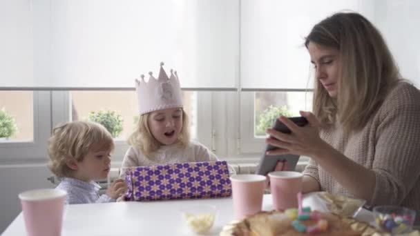 正の母と娘でカジュアル服で一緒に座ってテーブルでビデオ通話をしながら 誕生日を祝います自宅 — ストック動画