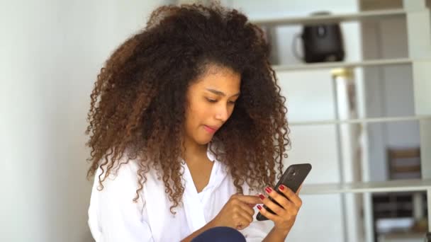 Mladá Afroameričanka Ležérní Oblečení Surfování Internetu Mobilním Telefonu Zatímco Odpočívá — Stock video