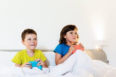 Evde yatak odasındaki battaniyenin altında birlikte rahat bir yatakta otururken oyun kağıtlarıyla oyun oynayan odaklanmış kardeşler.