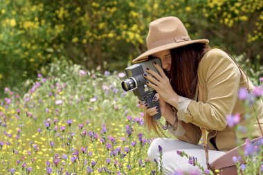 Kapalı gözlü bayan fotoğrafçı, güpegündüz çiçek açan ağaçların yanında dikilirken retro video kamerayla video kaydediyor.