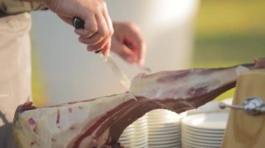 Tanınmaz hale gelmiş insan elleri ahşap bir jambon standından İspanyol jambonu kesiyor.