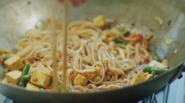 Mutfakta tavada soya peynirli ve sebzeli leziz erişteleri karıştıran yüzü olmayan bir kadının gerçek zamanı.