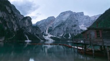 Berrak gölün kıyısındaki ahşap evin görkemli manzarası. Turkuaz su ve sabah vakti dağların arka planında yüzen kayıklar.