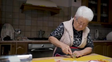 Mutfaktaki masada geleneksel tortellini pişirirken hamuru kesen yaşlı bir kadın.