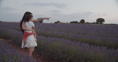 Tanımlanamayan, sevgi dolu bir annenin kucağına aldığı, elinde mor lavanta çiçekleriyle çiçek açan bir tarlada durup günbatımının tadını çıkarırken,